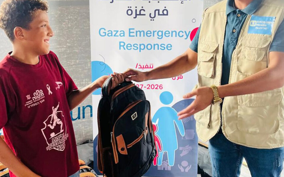 en pojke tar emot en ryggsäck av personal på SOS barnbyar i läger i gaza