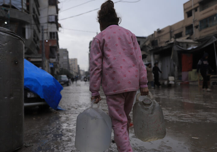 flicka i rosa kläder i gaza syns bakifrån bära tunga vattentankar